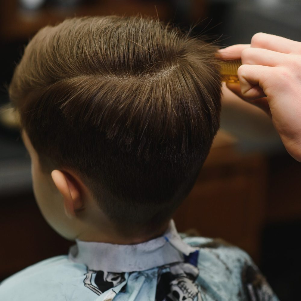 Cheerful Caucasian boy getting hairstyle in barbershop.