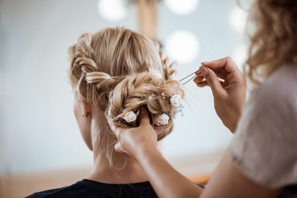 Female hairdresser making hairstyle to beautiful blonde girl in beauty salon. Copy space.